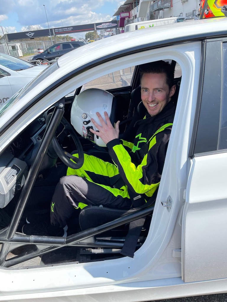 Christophe zwaait vanuit een racewagen op het circuit, helm in de andere hand